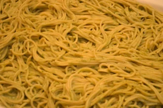 Plato de espagueti verde servido con queso parmesano encima
