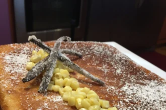 Porción de pan de elote decorado con granos de elote y azúcar glass, acompañado de salsa de rompope