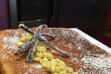 Porción de pan de elote decorado con granos de elote y azúcar glass, acompañado de salsa de rompope
