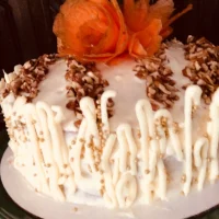 Pastel de zanahoria tropical decorado con nuez molida, zanahoria caramelizada y detalles de chocolate blanco, listo para servir.