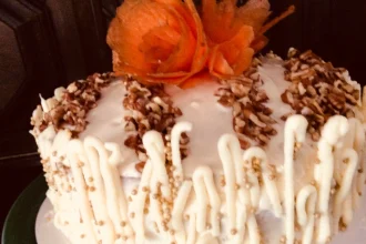Pastel de zanahoria tropical decorado con nuez molida, zanahoria caramelizada y detalles de chocolate blanco, listo para servir.