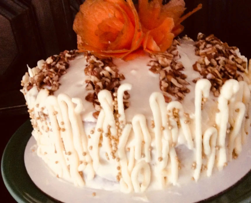 Pastel de zanahoria tropical decorado con nuez molida, zanahoria caramelizada y detalles de chocolate blanco, listo para servir.
