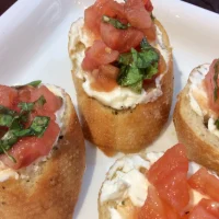 Bruschettas italianas sobre tabla de madera con tomates, queso feta y albahaca fresca