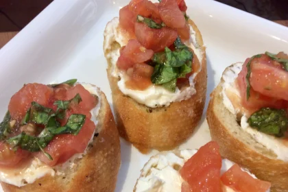 Bruschettas italianas sobre tabla de madera con tomates, queso feta y albahaca fresca