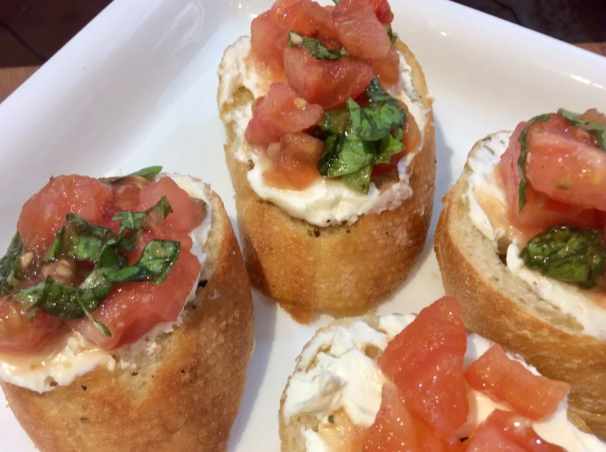 Bruschettas con tomates y quesos cremosos 1 Bruschettas italianas sobre tabla de madera con tomates, queso feta y albahaca fresca