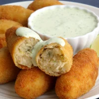 Plato con croquetas doradas de bacalao acompañadas de alioli de cilantro en un recipiente decorativo