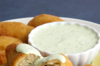Plato con croquetas doradas de bacalao acompañadas de alioli de cilantro en un recipiente decorativo