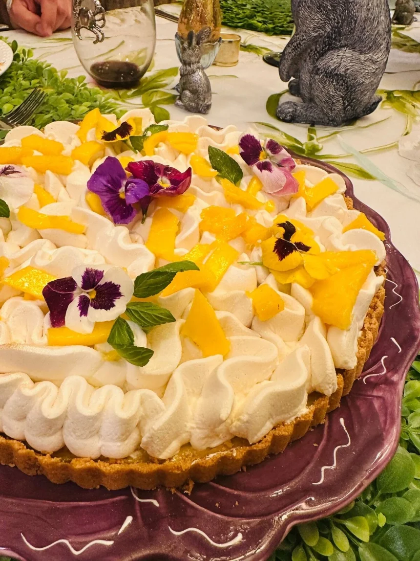 Pay de mango con base crujiente, relleno cremoso y decoración de crema batida, mango fresco y flores comestibles
