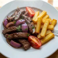 Lomo saltado peruano con salsa de soya oscura, papas crujientes al horno y verduras frescas en plato blanco, estilo casero y colores naturales.