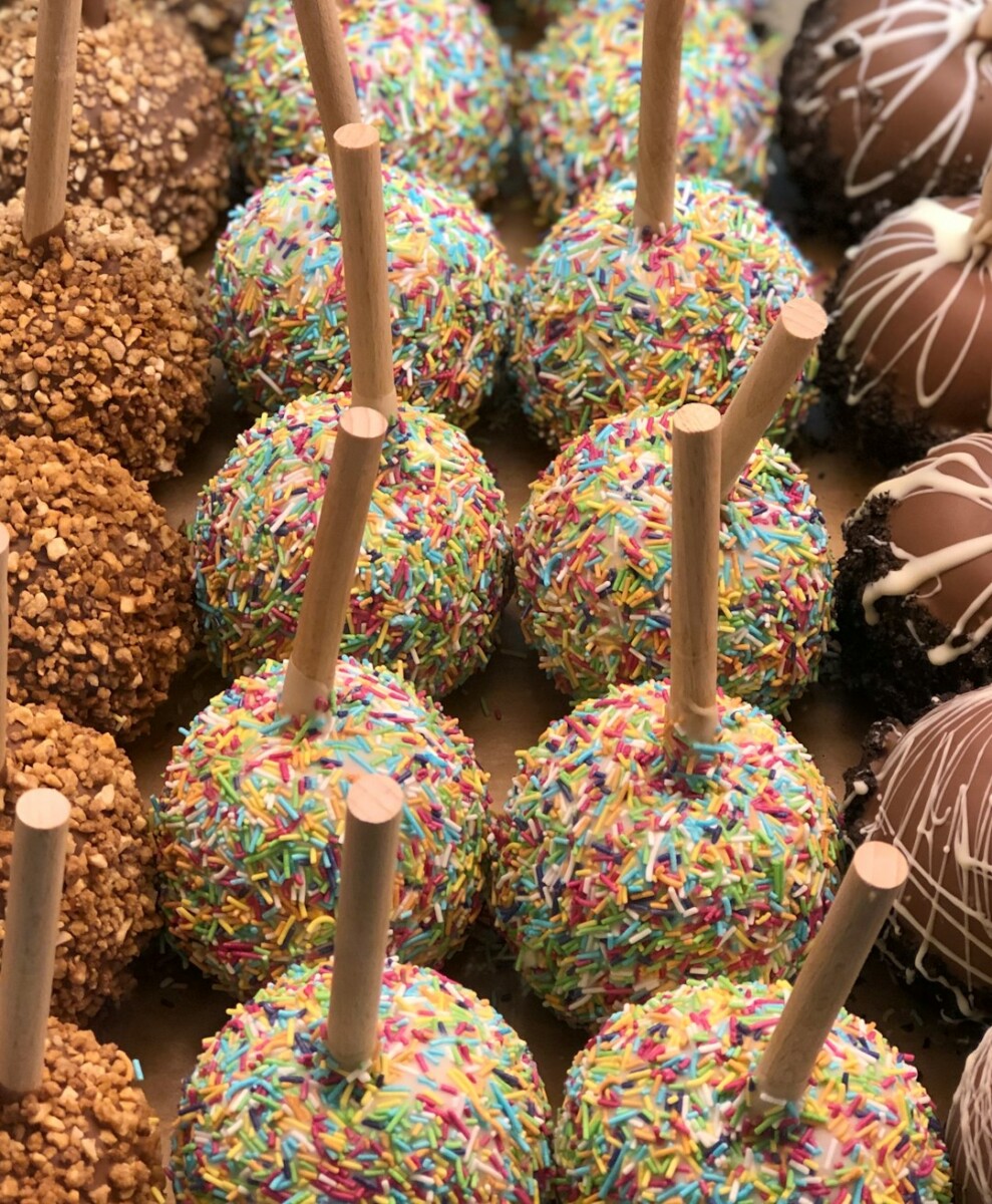 Manzanas rojas cubiertas de chocolate semiamargo con toppings de nuez, galleta triturada, chispas de colores y decoración de chocolate blanco en hilos